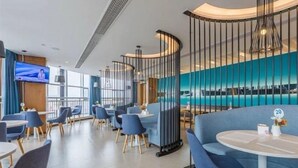 A modern hotel lobby with a curved seating area, a television screen, and a view of the pool. - Jinjiang Inn Select (Qingdao)