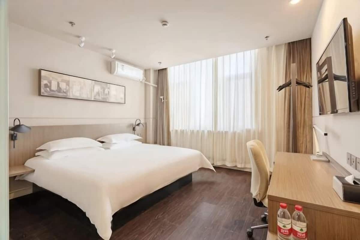 A hotel room with a bed, desk, chair, and large window with curtains.