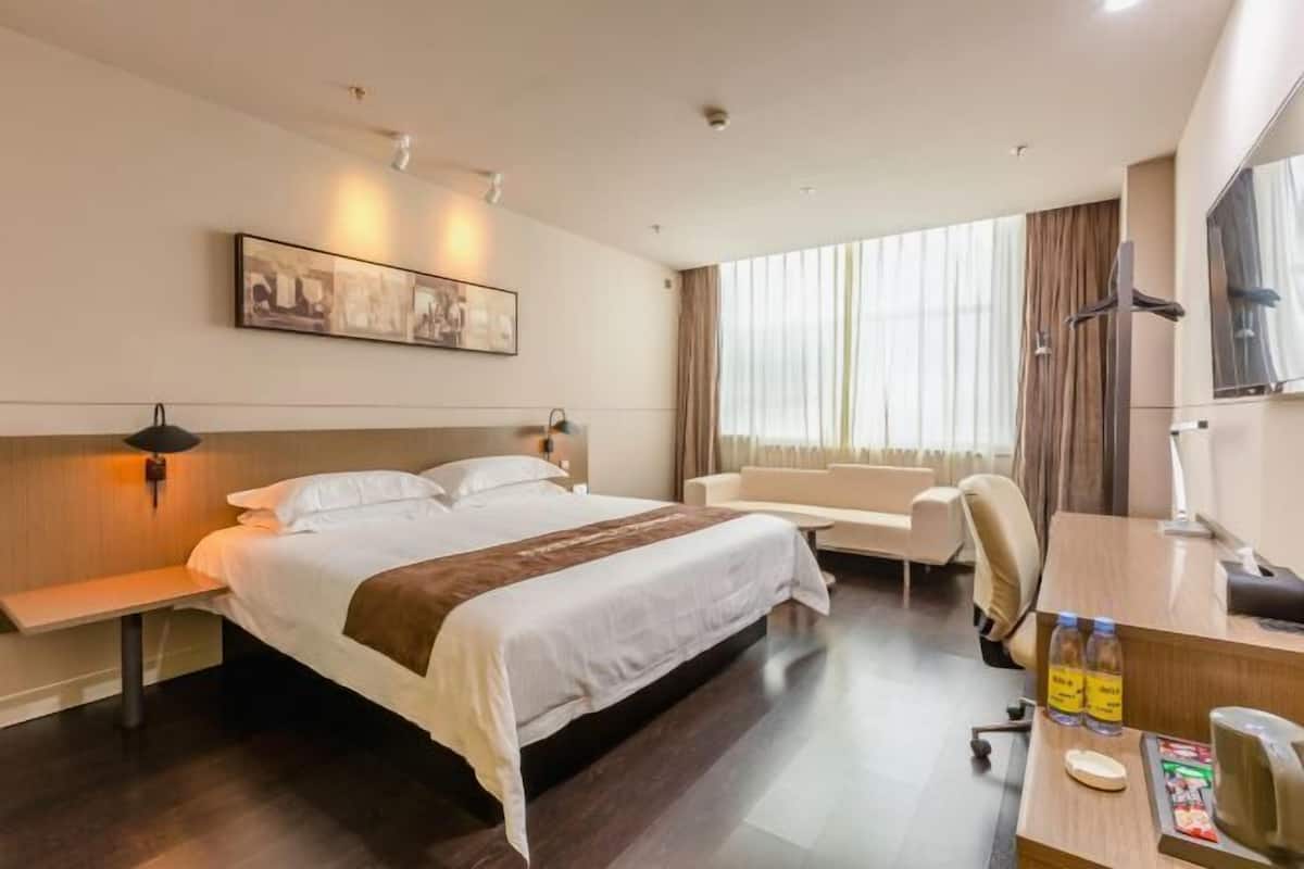 A hotel room with a large bed, a desk, a chair, a sofa, and a painting on the wall.