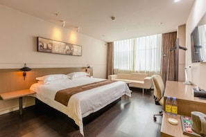 A hotel room with a large bed, a desk, a chair, a sofa, and a painting on the wall. - Jinjiang Inn Select (Qingdao)