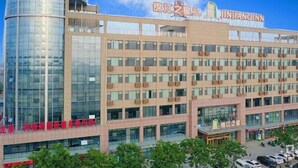 A multi-story hotel with a prominent cylindrical glass tower, multiple balconies, and a clear sky. - Jinjiang Inn Select (Qingdao)