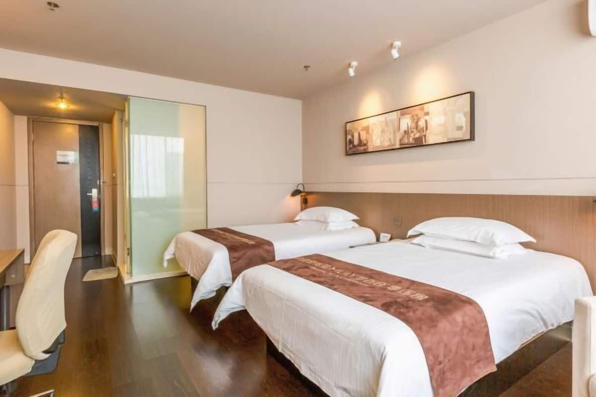 A hotel room with two beds, a desk, and a chair. There is a door leading to another room and a wall-mounted picture.