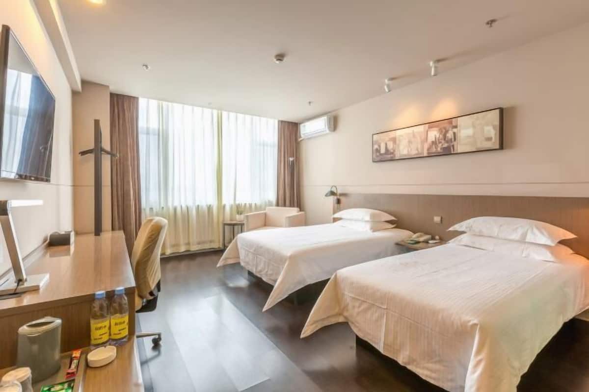 A hotel room with two beds, a desk with a computer, a chair, a TV, and a window with curtains.