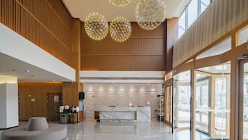 A spacious lobby with a reception desk, modern chandeliers, and a large glass entrance.