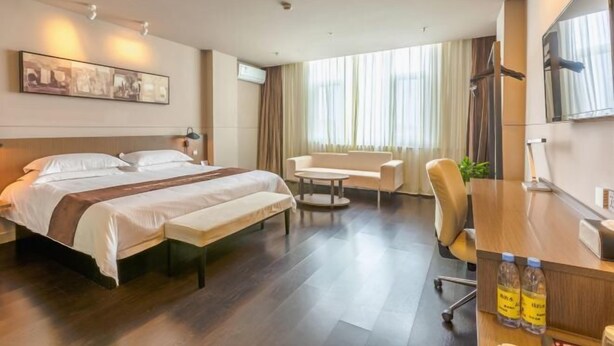 A hotel room with a bed, a sofa, a desk, and a large window with curtains. - Jinjiang Inn Select (Qingdao)