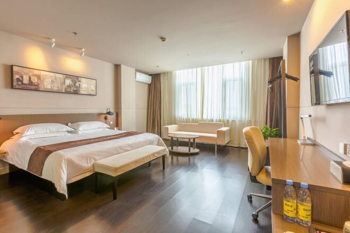 A hotel room with a bed, a sofa, a desk, and a large window with curtains.