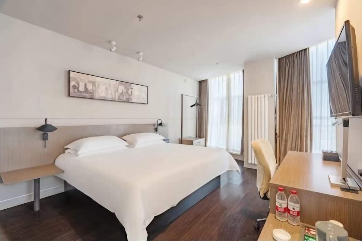 A hotel room with a bed, bedside table, desk, chair, TV, and a framed picture on the wall.