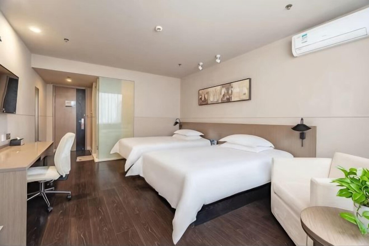 Una habitació d'hotel amb dos llits, un escriptori, una cadira, un sofà i una planta en test.