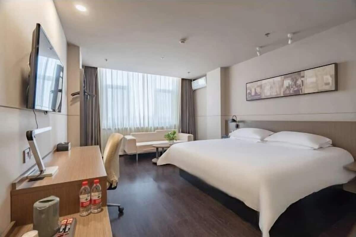 A hotel room with a large bed, a desk with a computer, a chair, and a TV.