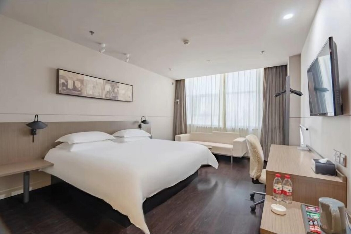 Habitació d'hotel moderna amb un llit gran, escriptori, cadira, televisió i finestra amb cortines.