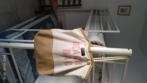 Un sac blanc sur lequel est écrit « SAC DE PLAGE », suspendu à un présentoir métallique blanc dans une pièce où se trouve un couvre-lit bleu à motifs.
