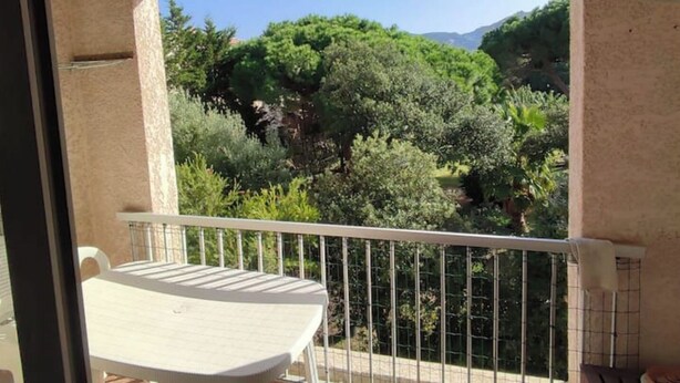 Un balcon avec une table et des chaises blanches, offrant une vue sur une végétation luxuriante et des arbres.