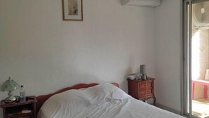Une chambre à coucher comprenant un lit, une table de chevet, une lampe, une paire de chaussons, un ventilateur de plafond et une fenêtre.