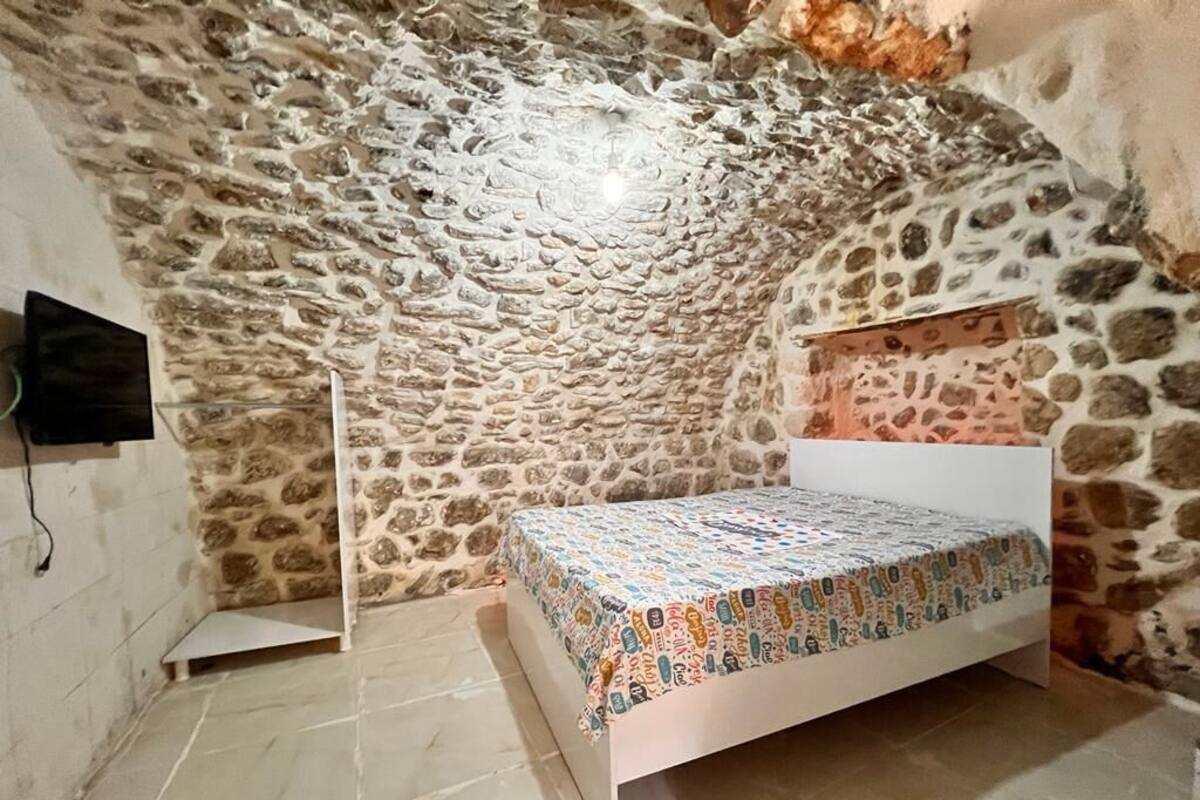 A bedroom with a stone ceiling, a bed with a patterned bedspread, and a television on the wall.
