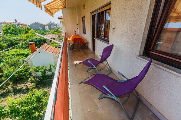 A balcony with two purple chairs, a small table with an orange tablecloth, and a window with curtains. - Apartment in Kaštel Novi with Terrace, Air condition, WIFI, Washing machine (5104-1) (Kaštel Novi)