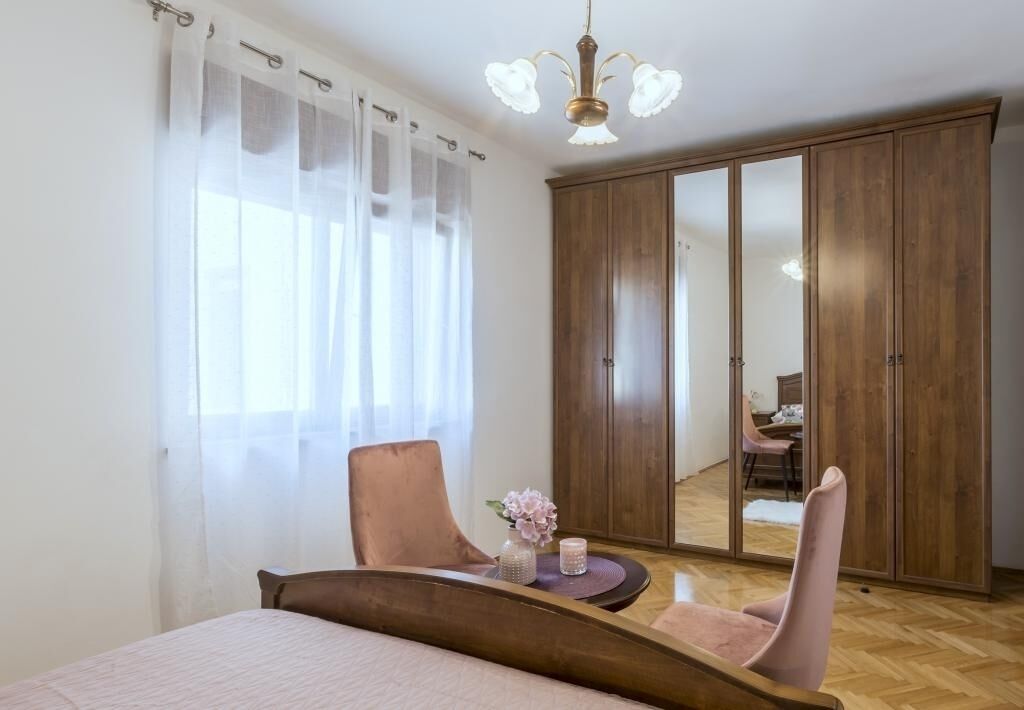 Quarto com cama, poltrona, mesa com vaso e vela, guarda-roupa e espelho.