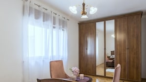 A bedroom with a bed, a chair, a table with a vase and candle, a wardrobe, and a mirror.