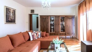 A living room with a sectional sofa, a glass coffee table with decorative items, a wooden cabinet, and a chandelier.