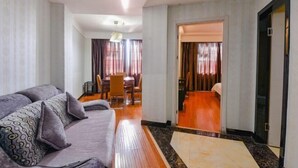 A hotel room with a sofa, a dining table, and a hallway leading to another room.