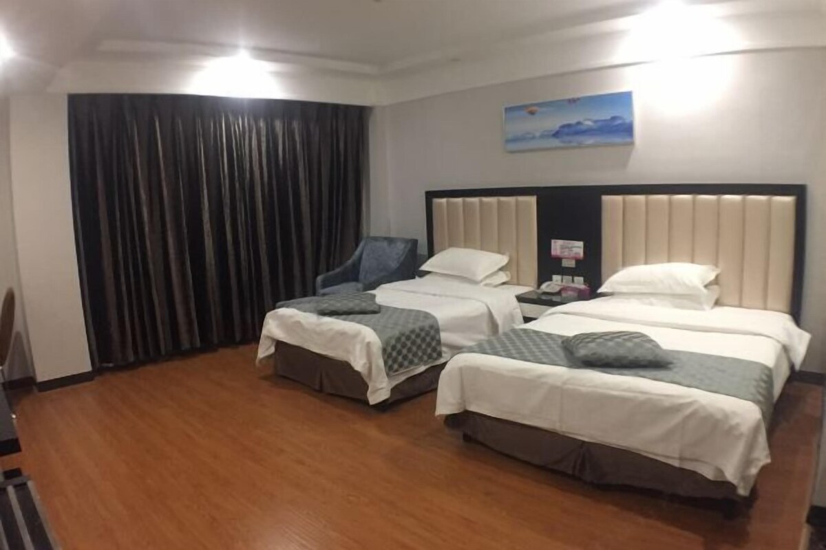 Habitación de hotel con dos camas, una silla, un escritorio, un cuadro en la pared y una cortina.