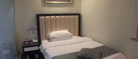 A single bed with a padded headboard, a bedside table with a lamp, and a framed picture on the wall.