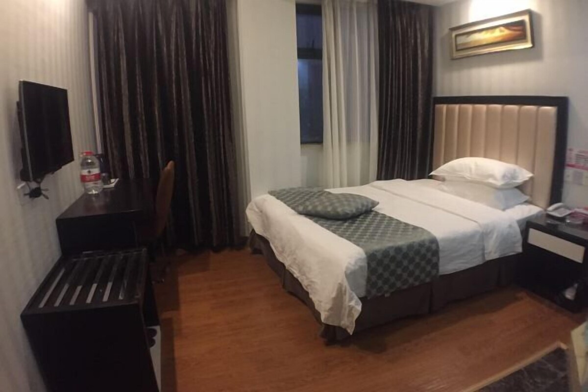 Una habitación de hotel con cama, escritorio, silla, televisor y cortinas.