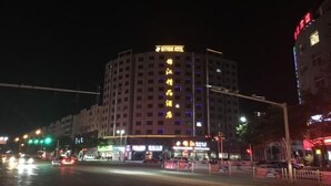 A multi-story hotel with illuminated signage, a prominent entrance, and a street view with traffic lights and vehicles.