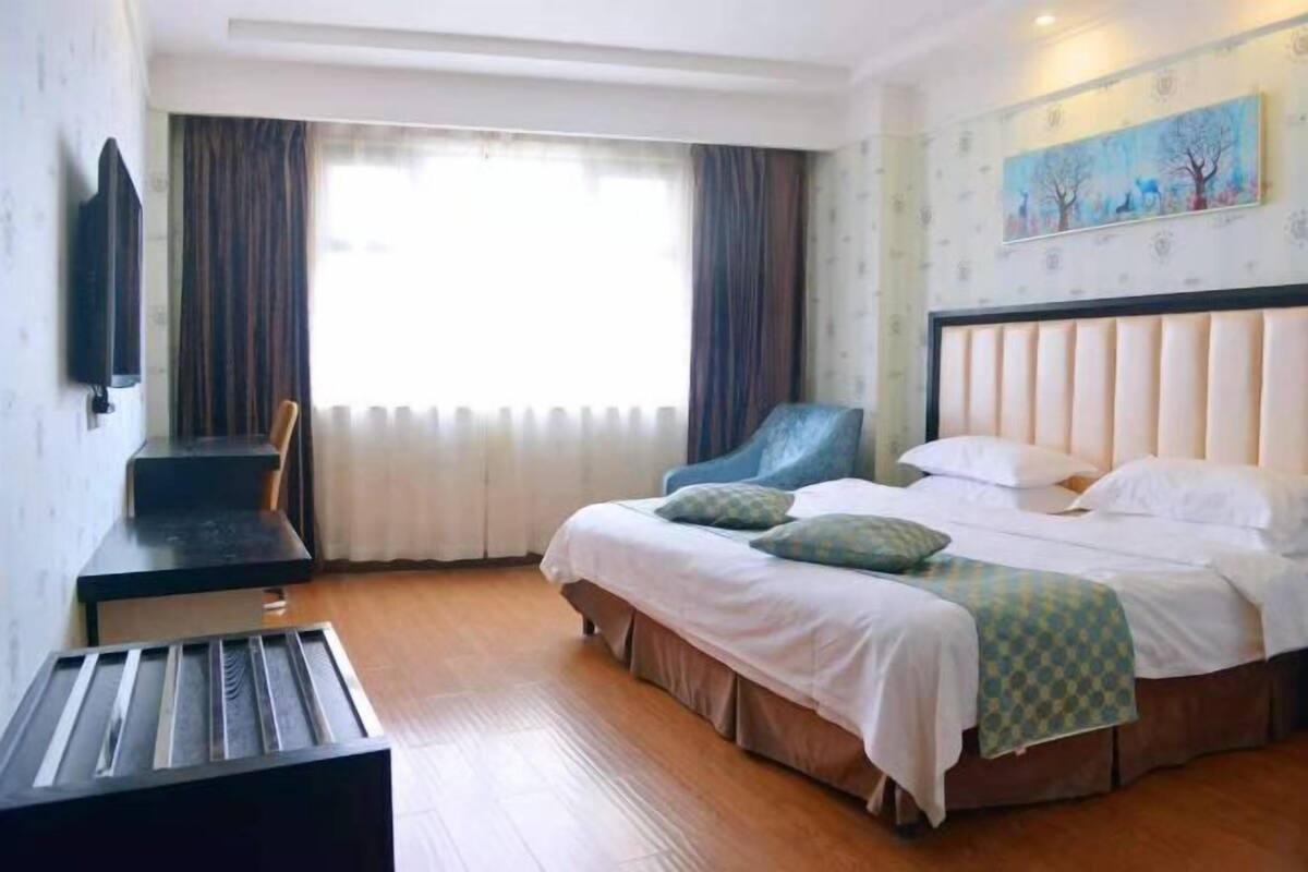 Una habitació d'hotel amb llit, escriptori, cadira, un quadre a la paret i finestra amb cortines.