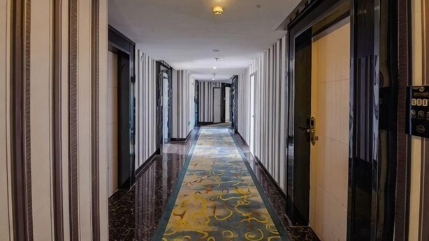 A long, narrow hotel corridor with a patterned carpet, doors on both sides, and a ceiling light.
