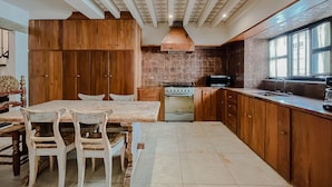 Una cocina con armarios de madera, una mesa de comedor con sillas, una estufa y una ventana con cortinas.