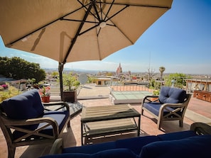 A terrace with outdoor seating, a large umbrella, and a view of a distant cityscape including a church.