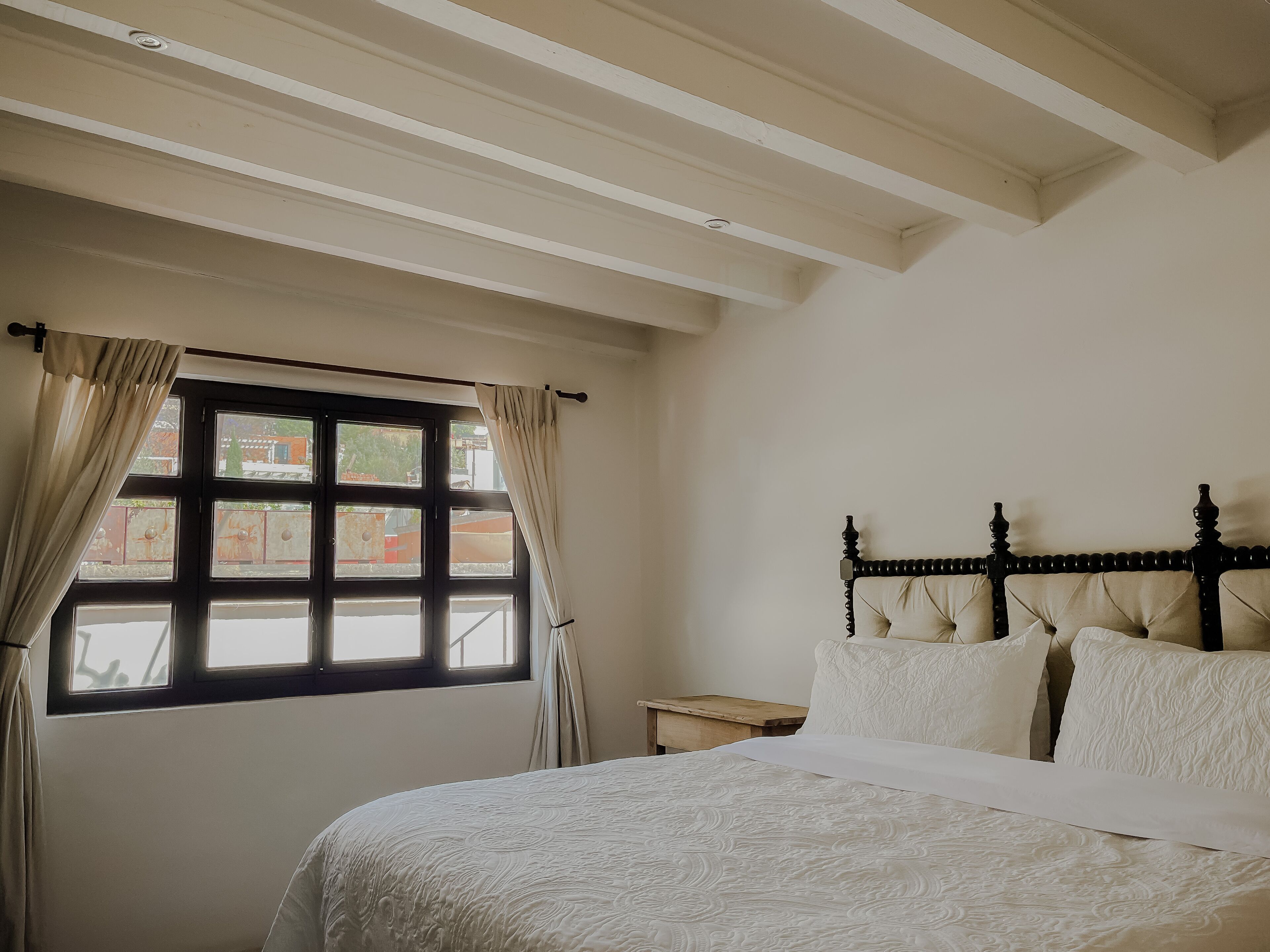 A bedroom with a large bed, a wooden headboard, and a window with curtains.