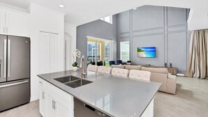 A modern kitchen with a large island, white cabinetry, and a stainless steel refrigerator. - Fantastic 5 Bedroom Champions Gate Resort Home With Spa and Pool (Davenport)