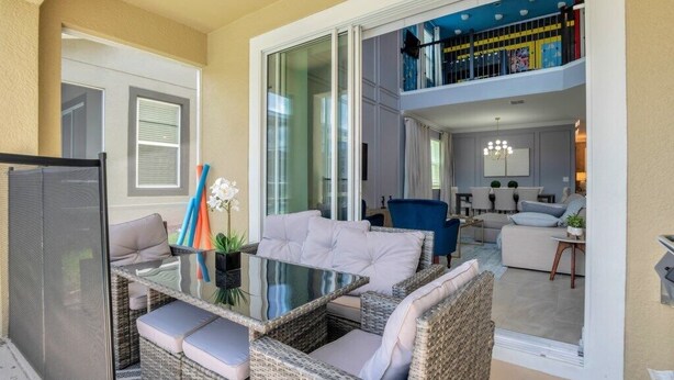 A modern living room with a glass dining table, wicker furniture, and a view of the upper floor. - Fantastic 5 Bedroom Champions Gate Resort Home With Spa and Pool (Davenport)