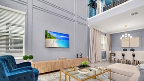 A spacious living room with a large TV, a sofa, a coffee table, and a dining area with a chandelier. - Fantastic 5 Bedroom Champions Gate Resort Home With Spa and Pool (Davenport)