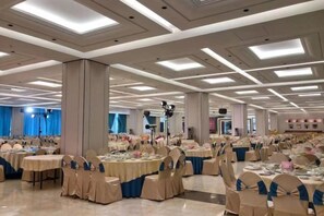 Un salón de banquetes con varias mesas redondas, cada una cubierta con un mantel y rodeada de sillas.
