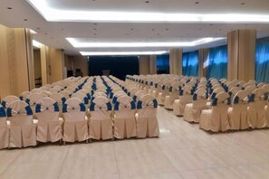 A large hall with rows of chairs covered in beige and blue, a stage at the front, and a modern ceiling with recessed lighting. - Master Hotel (Huidong)