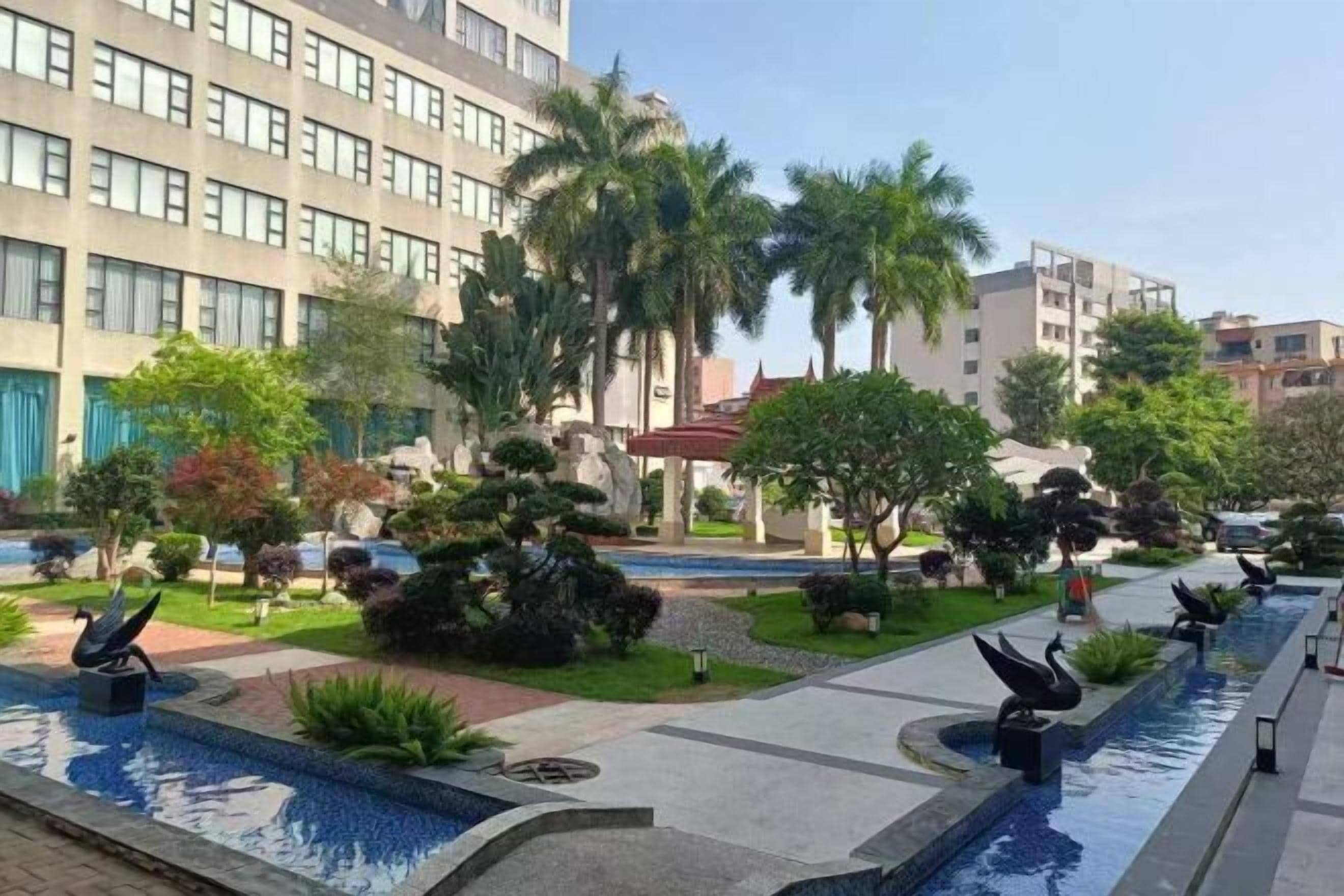 Un patio de hotel con fuente de agua, palmeras y un edificio moderno.