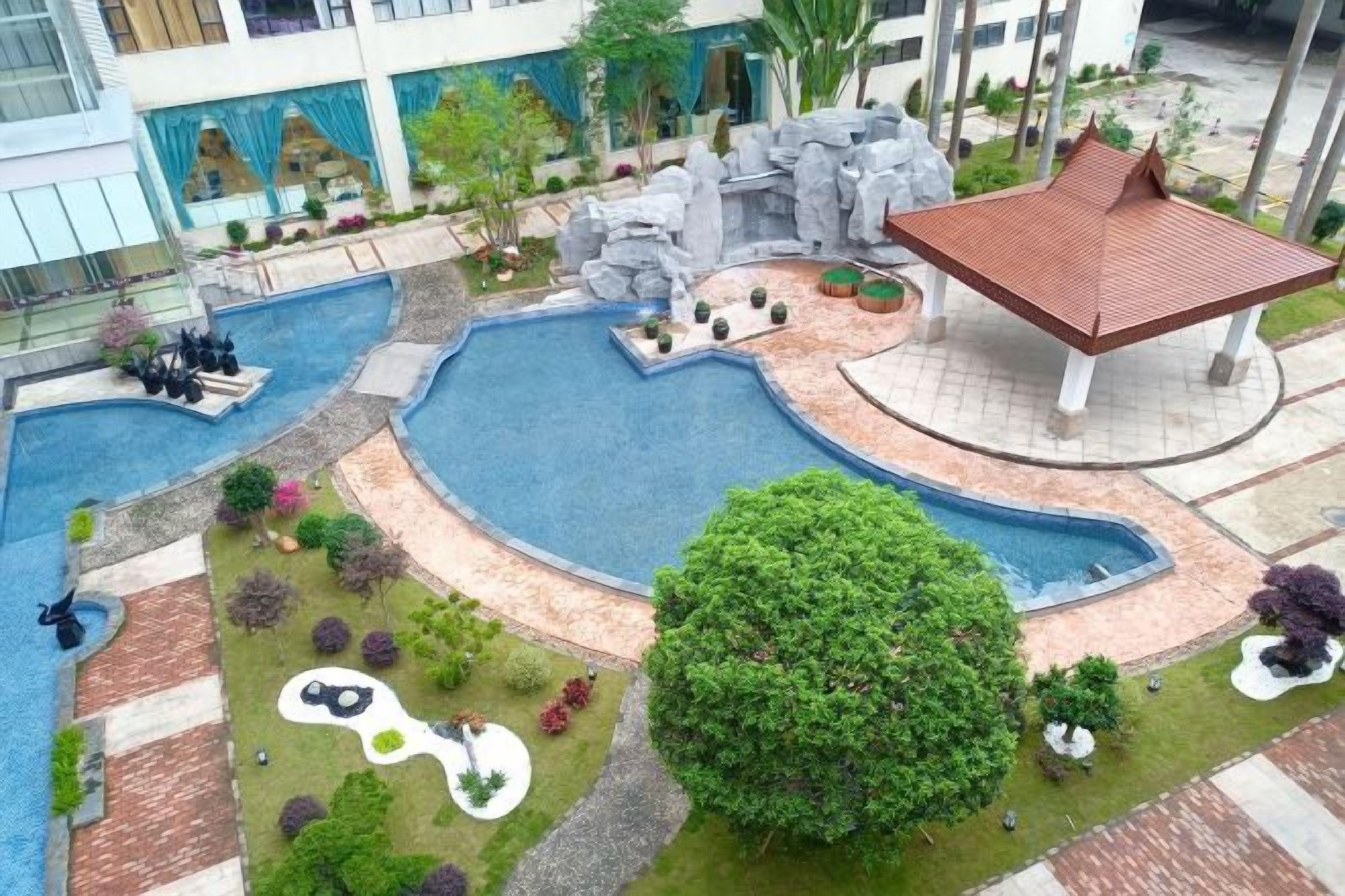 A landscaped pool area with a central water feature, surrounded by various plants and a gazebo.