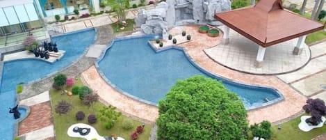 Zona de piscina ajardinada con un elemento central de agua, rodeada de plantas diversas y un pabellón.