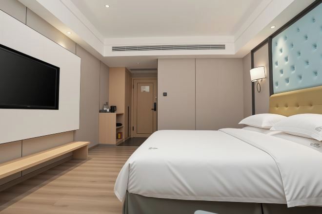 Una habitación de hotel moderna con un televisor de pantalla plana grande, un cabecero capitonado, una mesita de noche y una puerta que da a un baño.