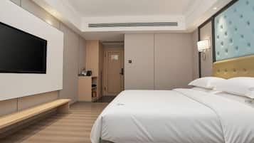 Una habitación de hotel moderna con un televisor de pantalla plana grande, un cabecero capitonado, una mesita de noche y una puerta que da a un baño.