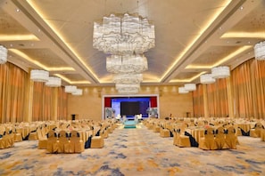 A large conference room with rows of chairs, a stage, and a chandelier. - Master Hotel (Huidong)
