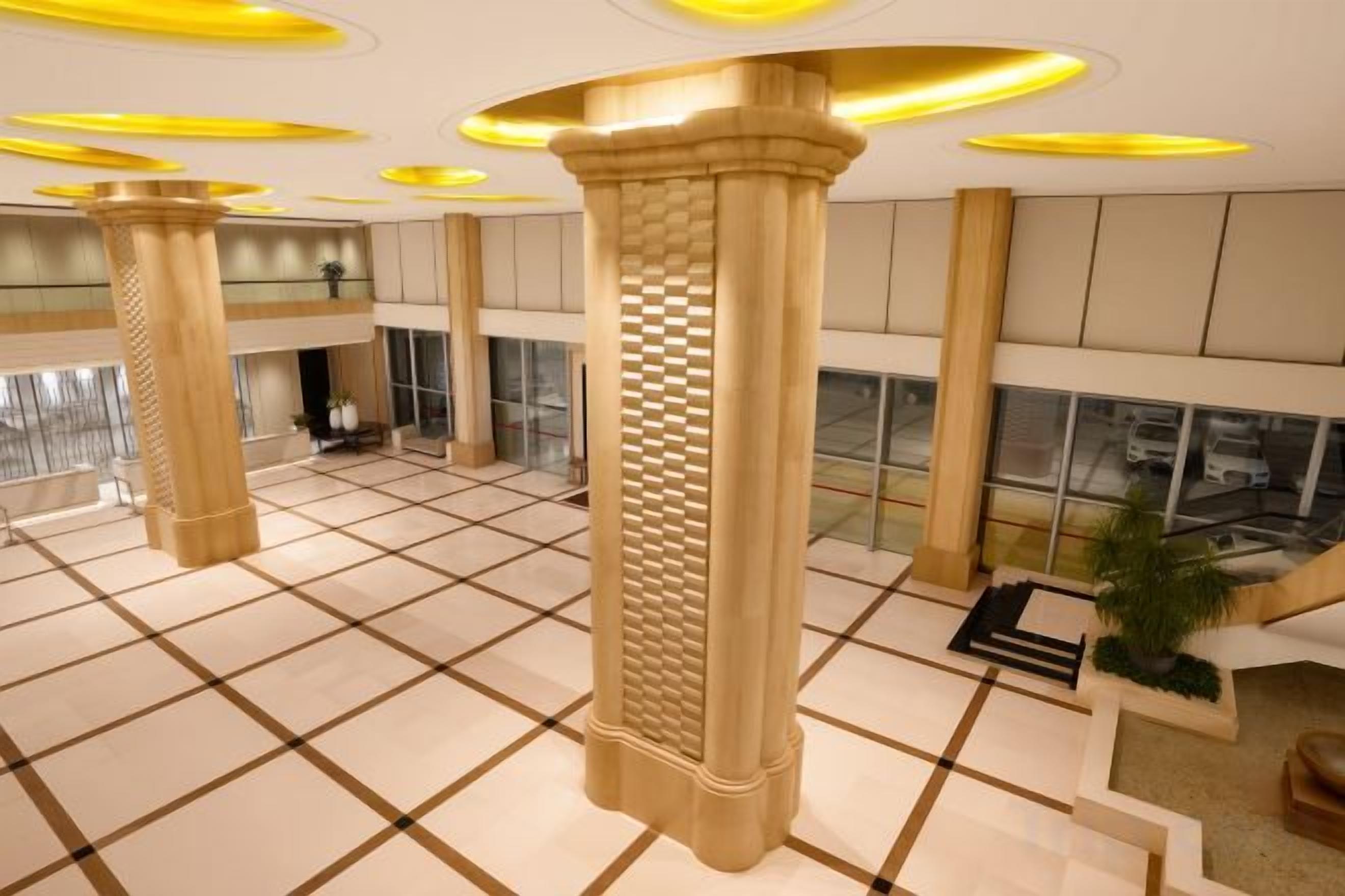 A spacious lobby with large columns, a checkered floor, and a view of the parking area through large windows.