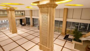 A spacious lobby with large columns, a checkered floor, and a view of the parking area through large windows.