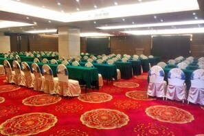 Een congreszaal met rijen tafels en stoelen, een rood tapijt en een podium.