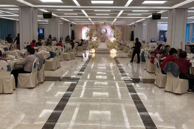A banquet hall with rows of tables and chairs, a central aisle, and a decorative floral arrangement at the end.