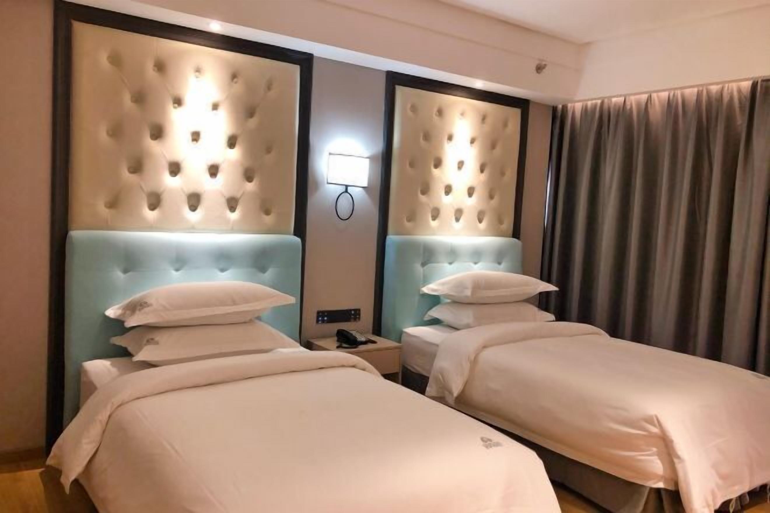 Une chambre d’hôtel avec deux lits, une tête de lit bleu clair, une lampe fixée au mur et un rideau.