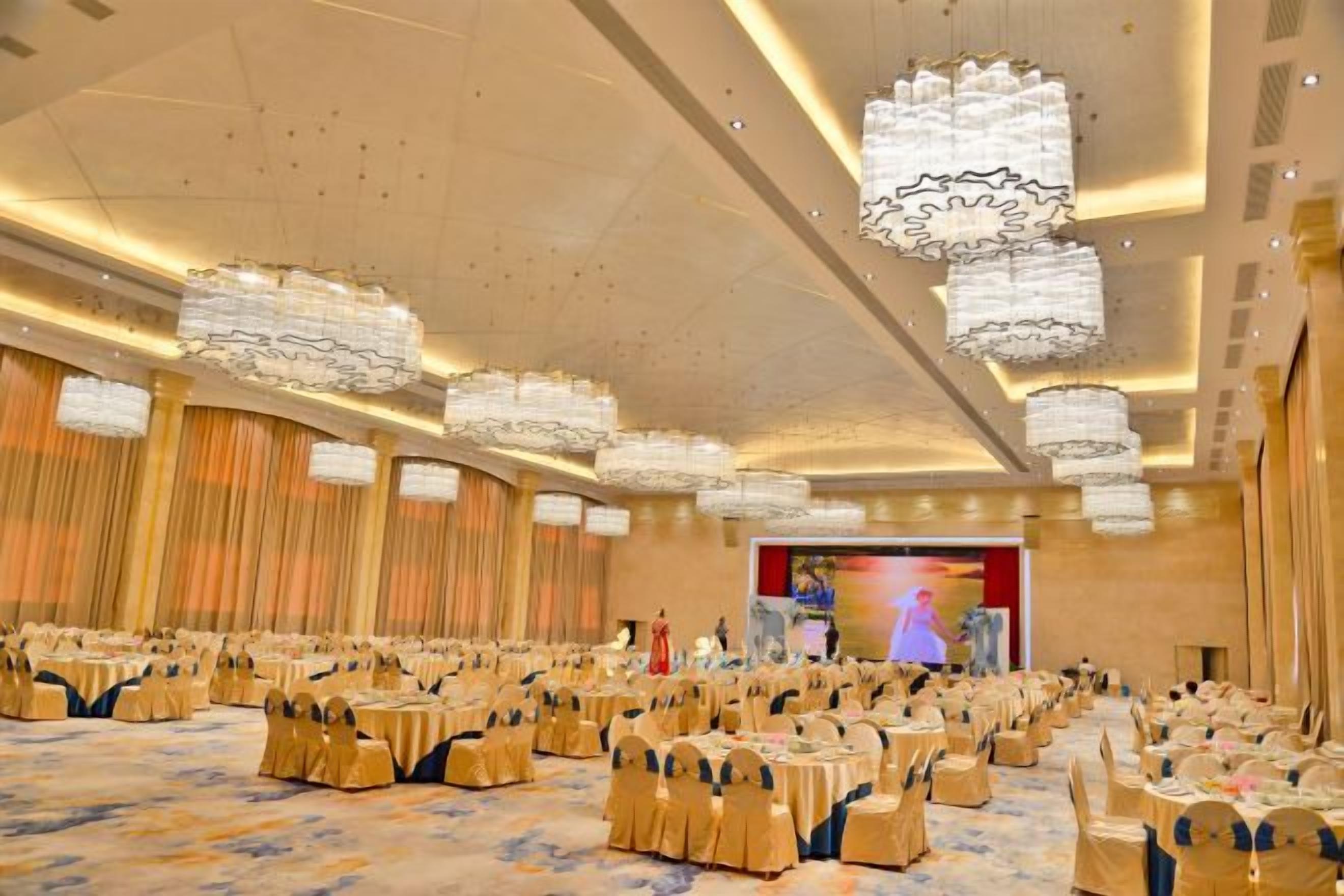 A banquet hall with round tables, chandeliers, and a stage.