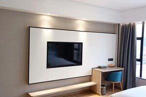 A modern hotel room with a large flat-screen TV mounted on the wall, a small desk with a chair, and a bed with a headboard. - Master Hotel (Huidong)